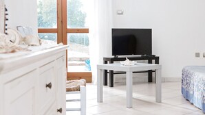 Une chambre moderne avec une commode blanche, un téléviseur posé sur un meuble noir, une table blanche et un lit recouvert d’une couverture à motifs.