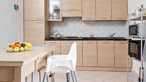 Une cuisine moderne avec des meubles en bois clair, un plan de travail blanc et un coin repas agrémenté d’une chaise blanche.