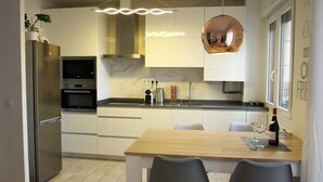 Une cuisine moderne dotée d’appareils électroménagers en acier inoxydable, d’une table à manger en bois et d’un luminaire suspendu en cuivre.