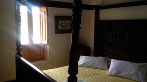 Un lit à baldaquin avec une tête de lit en bois, une fenêtre avec des rideaux et un tableau encadré accroché au mur.