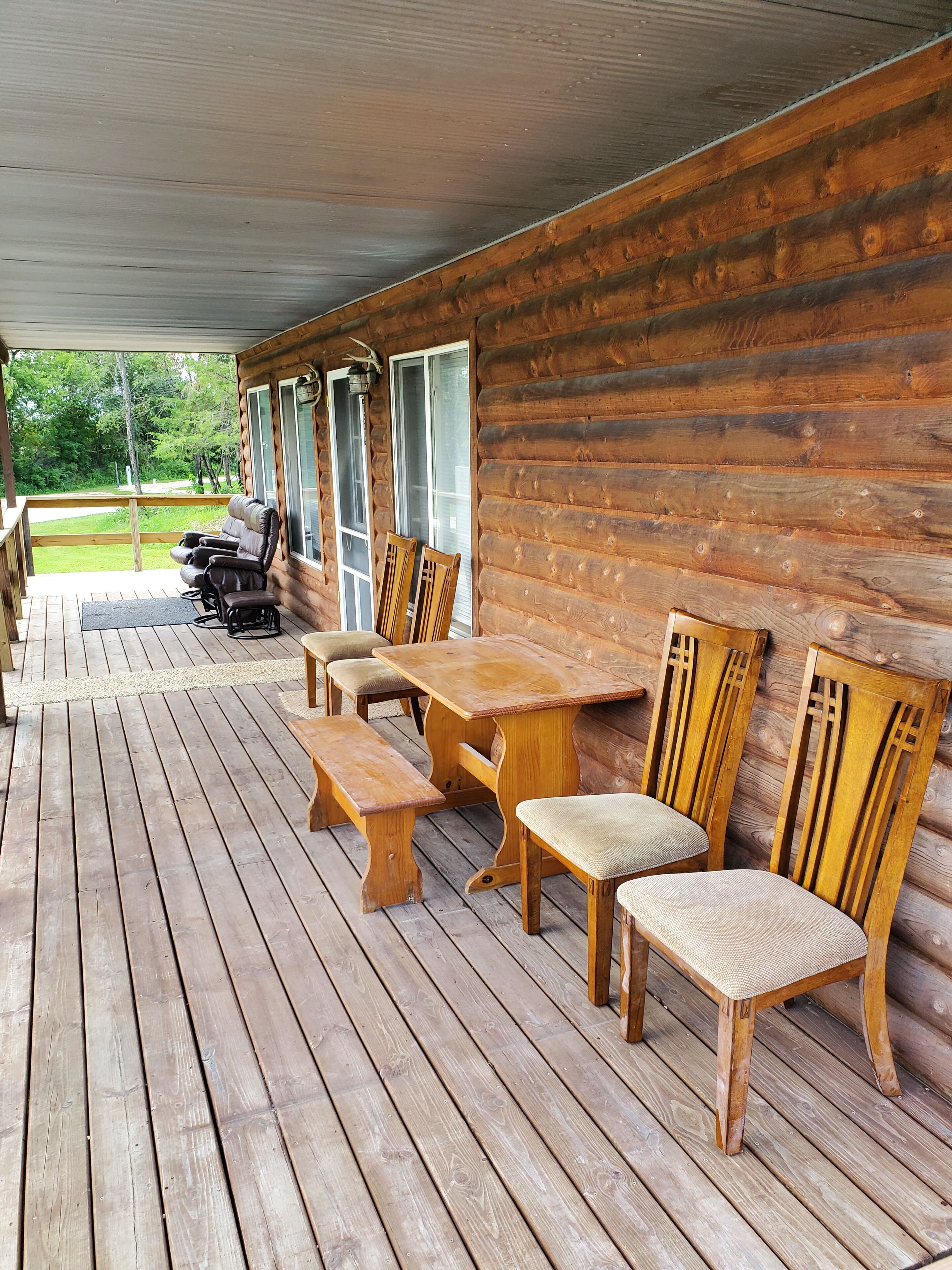 A wooden deck with a table and chairs, a bench, and a view of a green landscape.