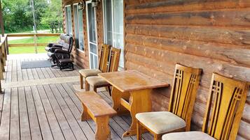 A wooden deck with a table and chairs, a bench, and a view of a green landscape.