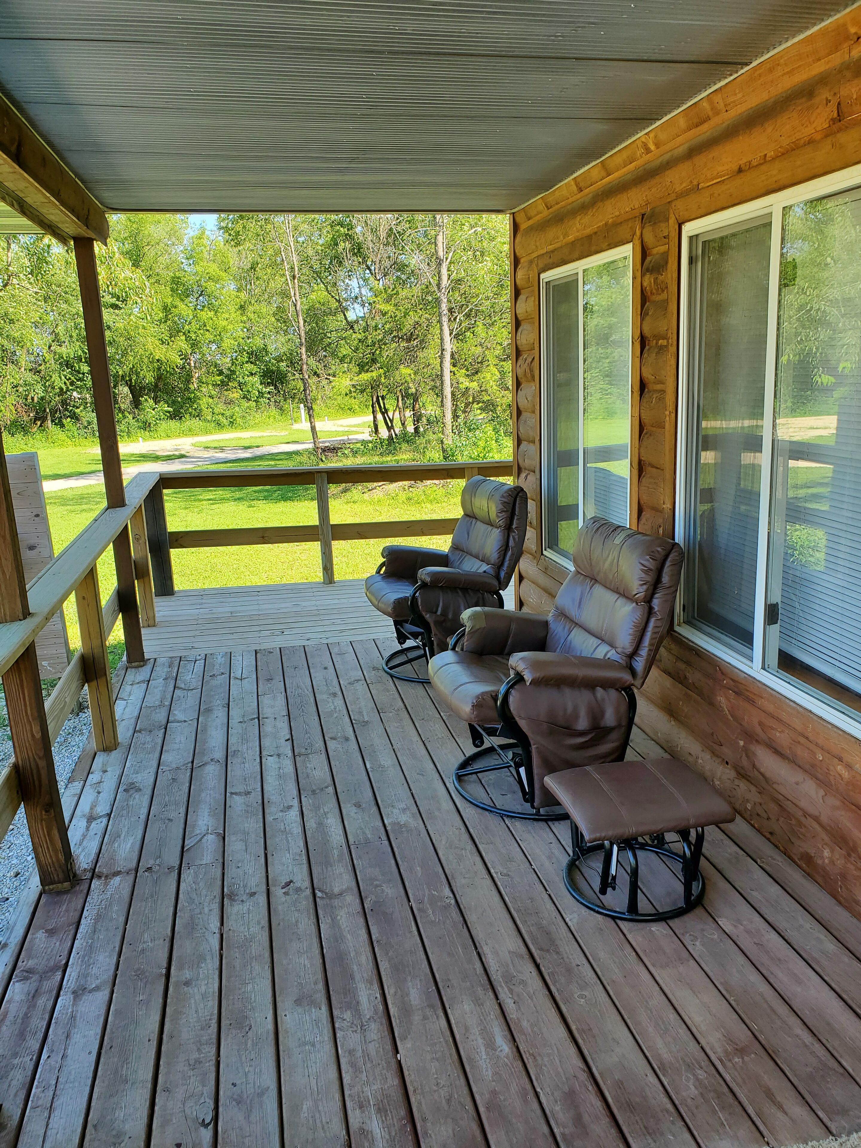 A wooden deck with three leather recliners and a bench, overlooking a green landscape.
