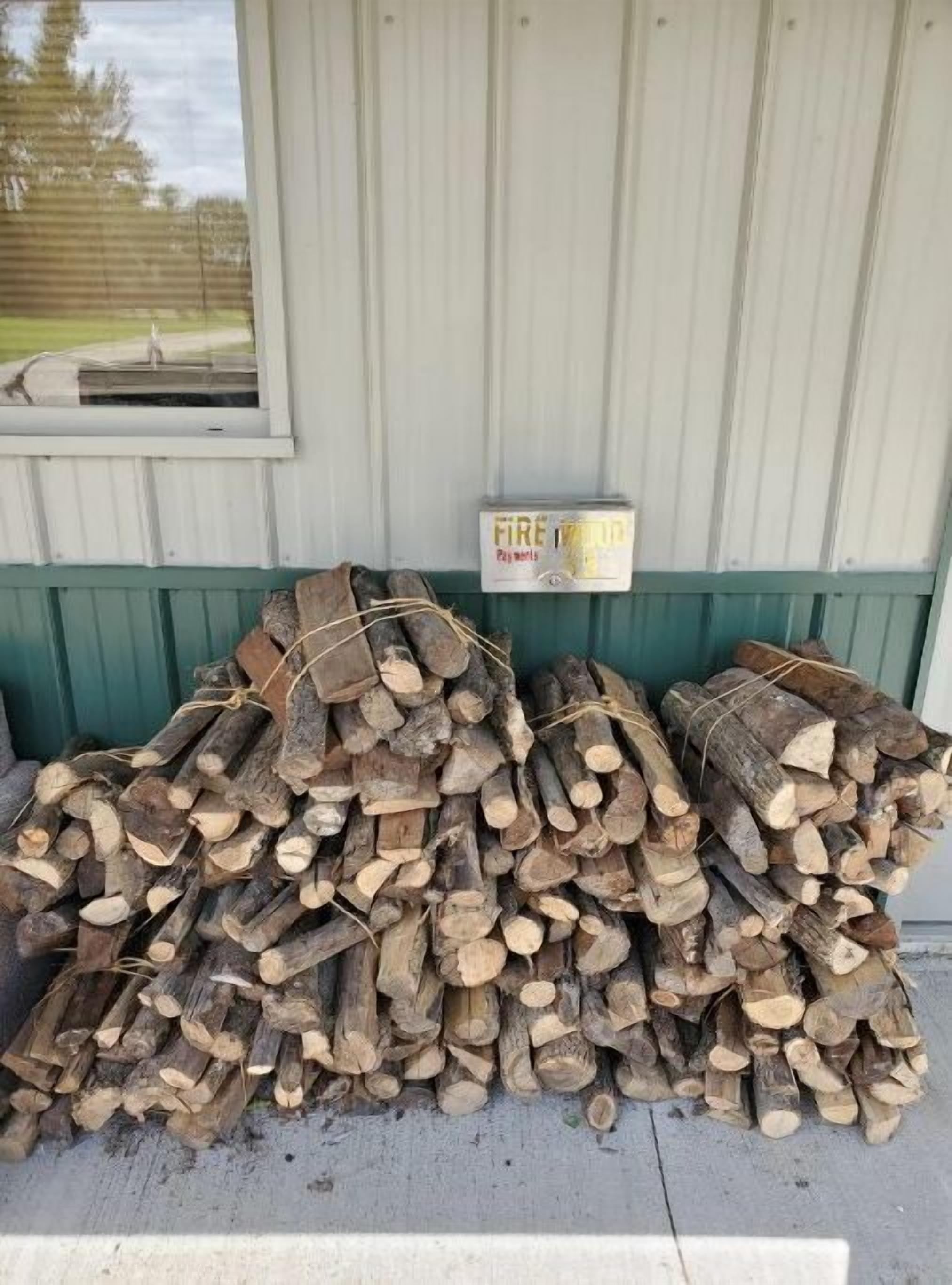 Ein Holzstapel vor einem Gebäude, an dem ein Schild mit der Aufschrift 'FIREWOOD' hängt.