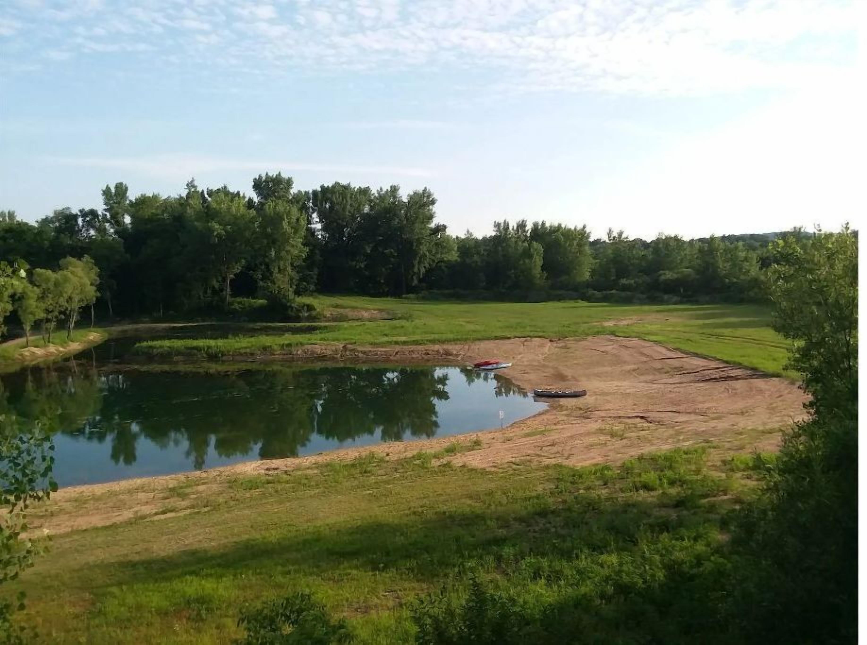 A natural landscape with a pond, grassy areas, and trees.