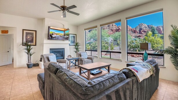 A living room with a fireplace, large windows with a desert view, a ceiling fan, and a sofa. - Experience luxury at Sedona Star View, a 3-bed home with stunning red rock views. (Sedona)