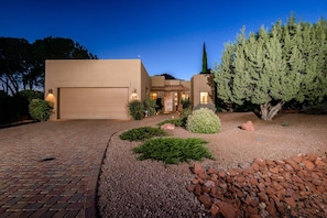 A modern house with a garage, a well-maintained garden with shrubs and rocks, and a tall tree.