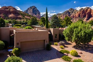 A residential area with modern architecture, a paved driveway, and a view of red rock formations in the background.