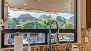 Una cocina con un lavamanos, una ventana con vistas a un jardín y una vista de un paisaje montañoso.