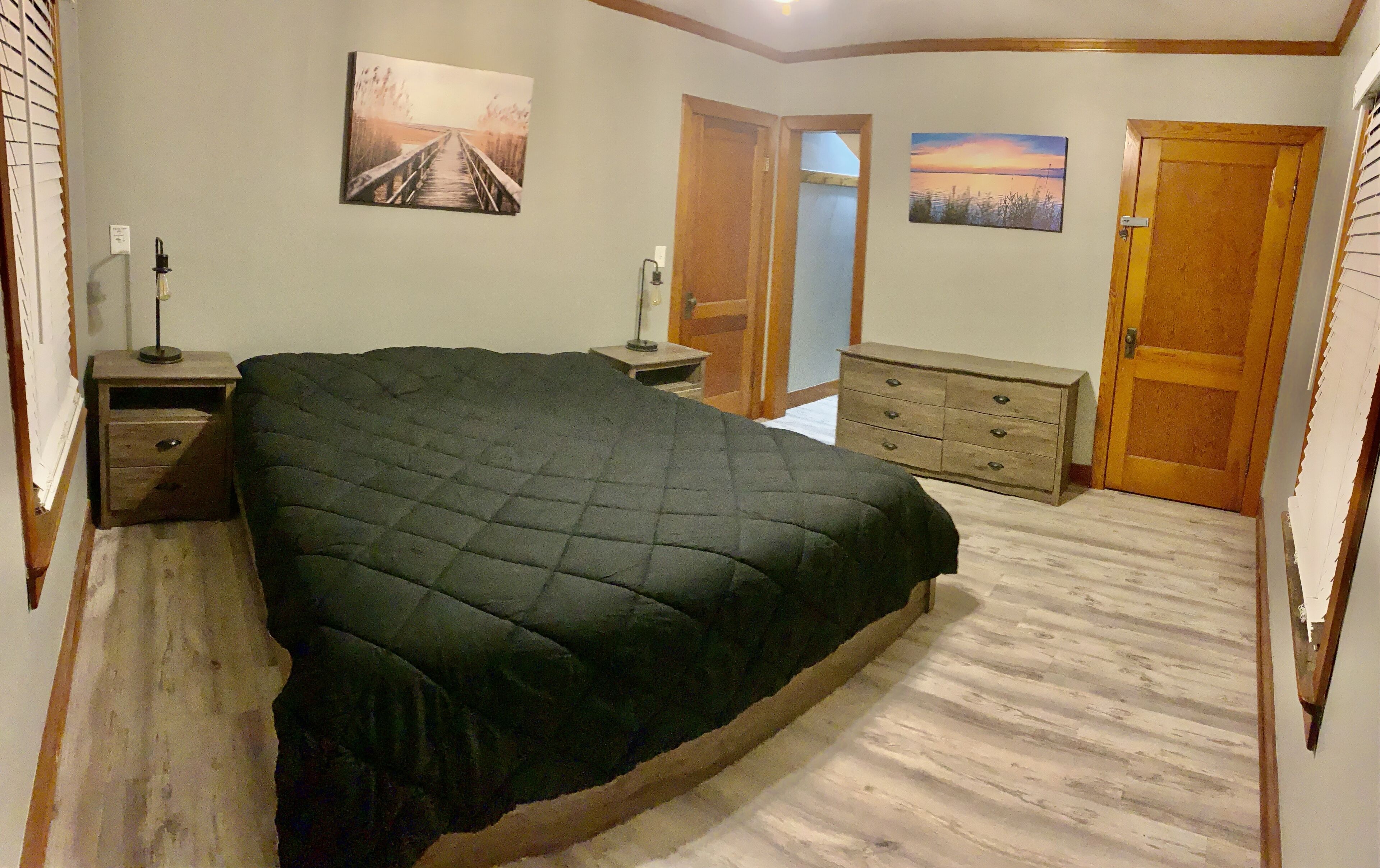 A bedroom with a large bed, a nightstand, a dresser, and two doors.