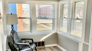 Une pièce d’angle avec un plafond en pente, de grandes fenêtres, un radiateur et une chaise.