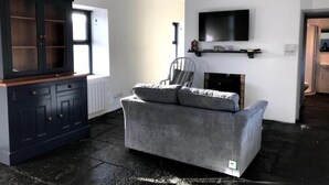 Un salón con un aparador azul oscuro, un sofá gris, un televisor montado en la pared y una chimenea.