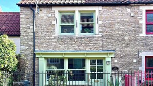 A stone building with a green door and windows, a metal gate, and a red door in the background. - Apple Cottage - Central Frome - Family Friendly (Somerset)