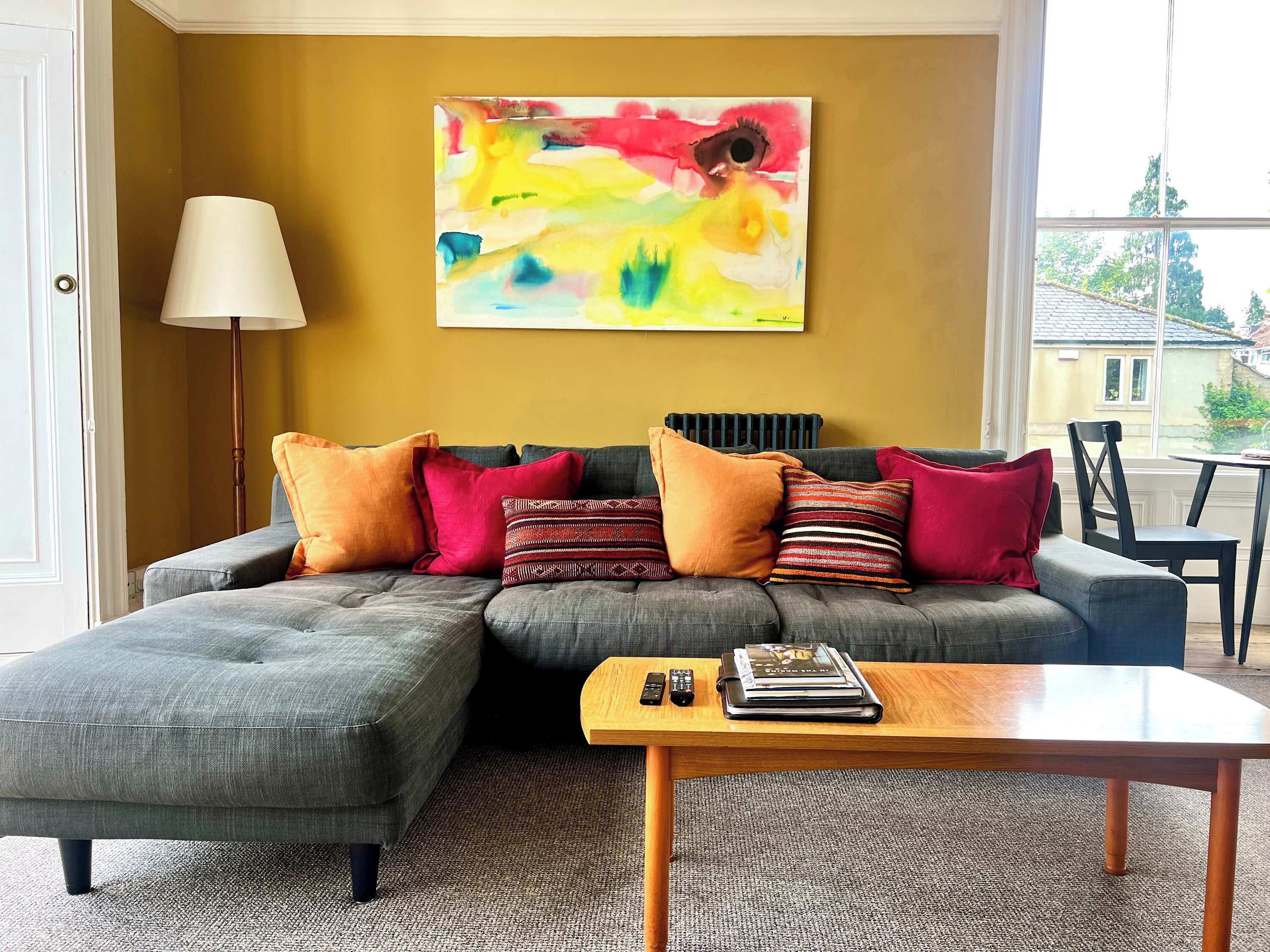 Una sala de estar con un sofá modular, una mesa de centro y un cuadro abstracto de colores en la pared.