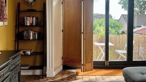 Ein Zimmer mit Holztür, Bücherregal und Blick auf einen Garten mit Zaun und Gartenmöbeln.