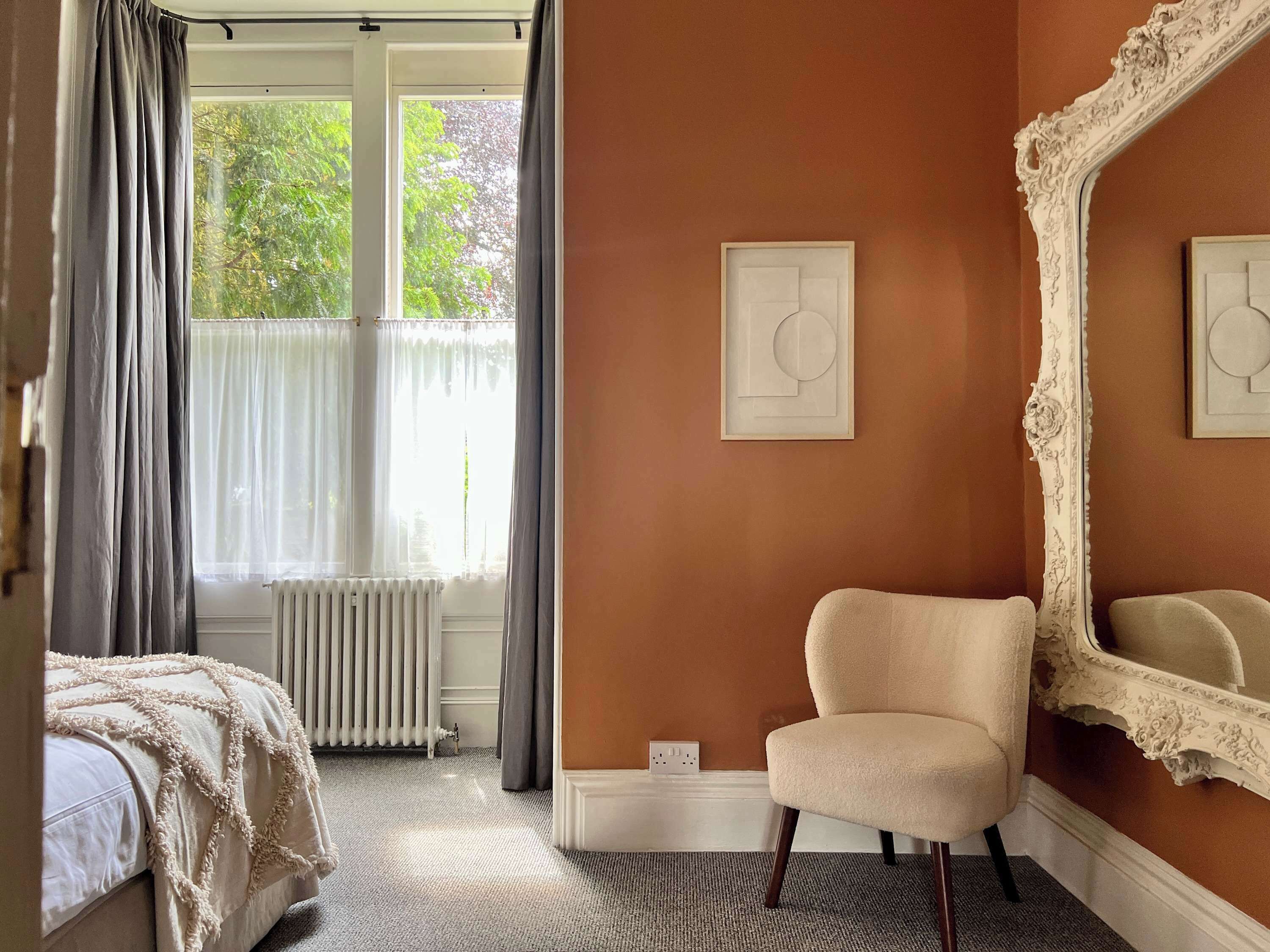 Ein Schlafzimmer mit großem Fenster, Heizkörper, Stuhl und Spiegel.