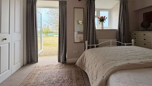 A bedroom with a bed, a dresser, a mirror, and a window with curtains. - The View Cottage -Tennis Court- Nr Frome, Longleat (Nunney)