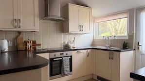 A modern kitchen with a stove, oven, and a window with a view of trees. - The View Cottage -Tennis Court- Nr Frome, Longleat (Nunney)