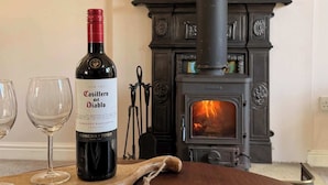 A bottle of Casillero del Diablo wine, two empty wine glasses, and a wood-burning stove in a room. - The View Cottage -Tennis Court- Nr Frome, Longleat (Nunney)