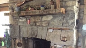 Une cheminée en pierre avec des étagères où sont disposés divers objets, un panier et une bouilloire.