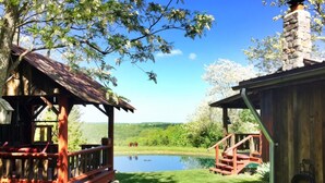 Un chalet rustique doté d’une terrasse en bois et d’une cheminée en pierre, offrant une vue sur un lac paisible et une végétation luxuriante.