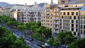 Un edificio de varios pisos con balcones, una calle con coches y árboles.