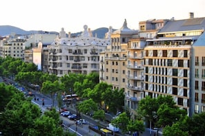 A multi-story building with balconies, a street with cars, and trees.
