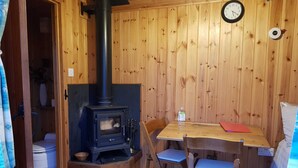 A cozy cabin with a wood-burning stove, a wooden dining table, and chairs. - Beavers Lodge on top of the Shropshire Hills (Craven Arms)