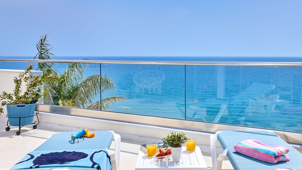 Un balcón con vista a la piscina, sillas de descanso, una mesita con una planta y una silla azul.