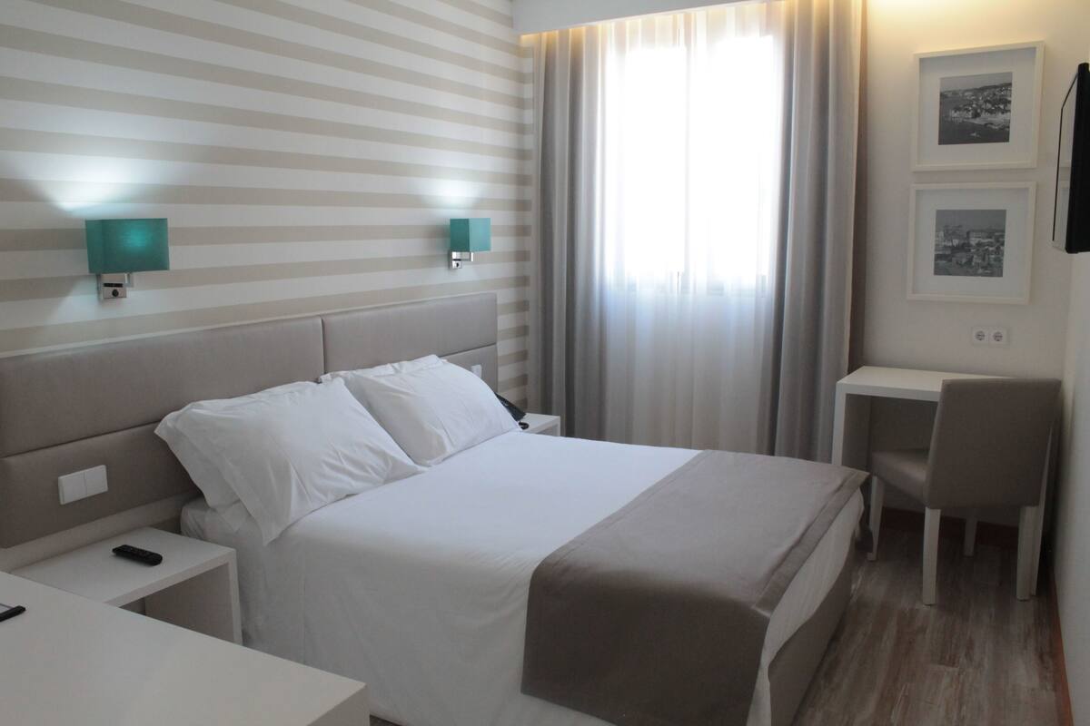 Una habitación de hotel con cama, mesitas de noche, escritorio y silla.