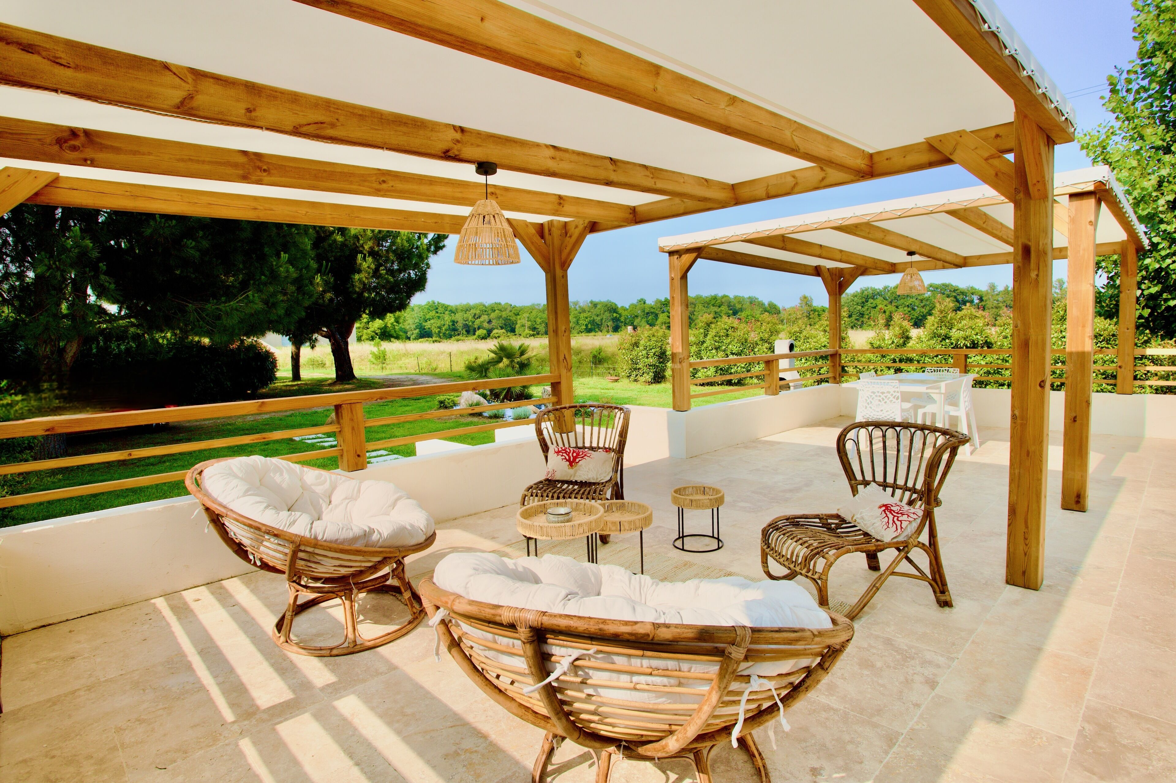 Une terrasse extérieure aménagée avec du mobilier en bois, notamment des fauteuils en osier et une table, donnant sur un jardin luxuriant.