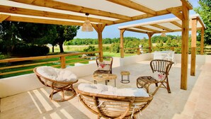 An outdoor patio with wooden furniture, including wicker chairs and a table, overlooking a lush garden. - Campo Vecchio Mare & Piscine (Ghisonaccia)