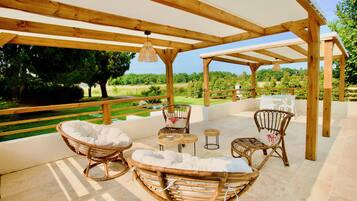Une terrasse extérieure aménagée avec du mobilier en bois, notamment des fauteuils en osier et une table, donnant sur un jardin luxuriant.