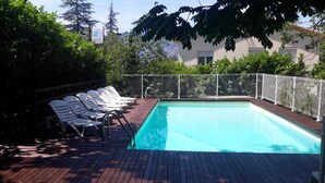 Ein rechteckiger Pool mit Holzdeck und Metallgeländer, umgeben von üppiger Vegetation und Bäumen.