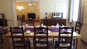 Een eetgedeelte met een grote houten tafel voor zes personen, omringd door houten stoelen. Een televisie is aan de muur bevestigd, en een vintage radio staat op een bijzettafeltje.