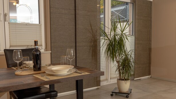 A dining area with a wooden table, chairs, a bottle of wine, and a potted plant.