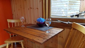 A wooden dining table with two chairs, a bowl of blue flowers, and two wine glasses. - Cabin Retreat With Beavers on Shropshire Hills (Craven Arms)