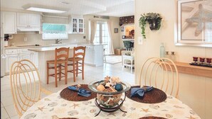 Een keuken met witte kasten, een eethoek met een tafel voor vier personen, en een woonkamer met een bank en een televisie.