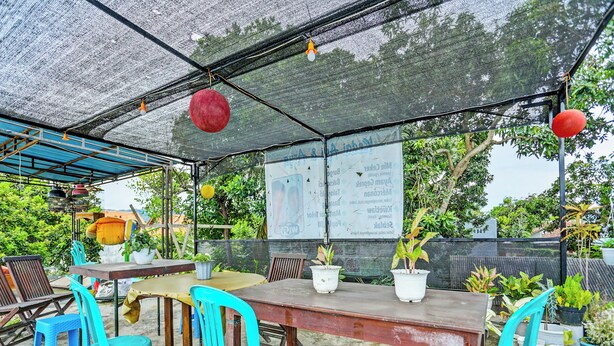 An outdoor seating area with tables and chairs, a covered section with a mesh roof, and potted plants. - OYO 3214 Puri Amalia (Banyuwangi)