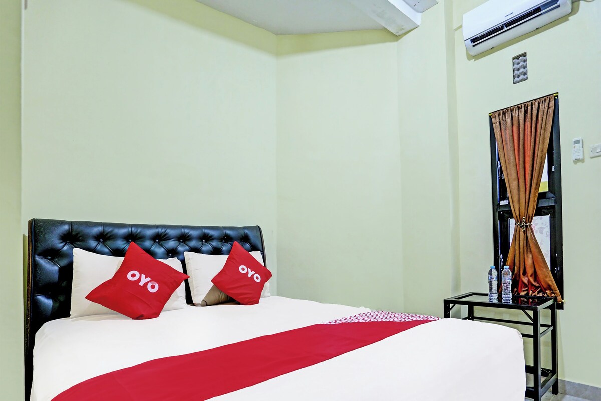 A hotel room with a bed, a black headboard, and a red and white bedspread.