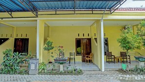 A covered porch with yellow walls, potted plants, and outdoor seating. - OYO 3214 Puri Amalia (Banyuwangi)