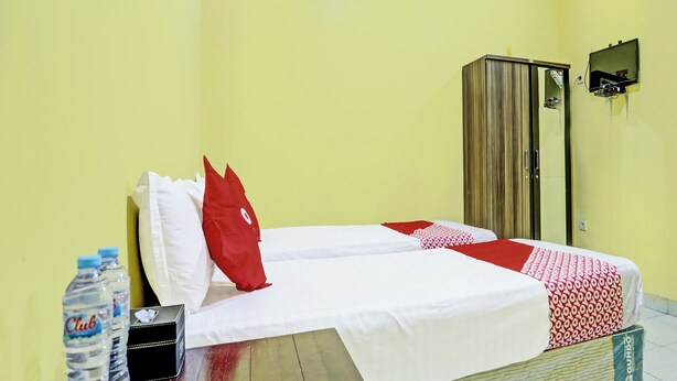 A hotel room with a bed, a wooden nightstand, a water bottle, a TV, and a wardrobe. - OYO 3214 Puri Amalia (Banyuwangi)