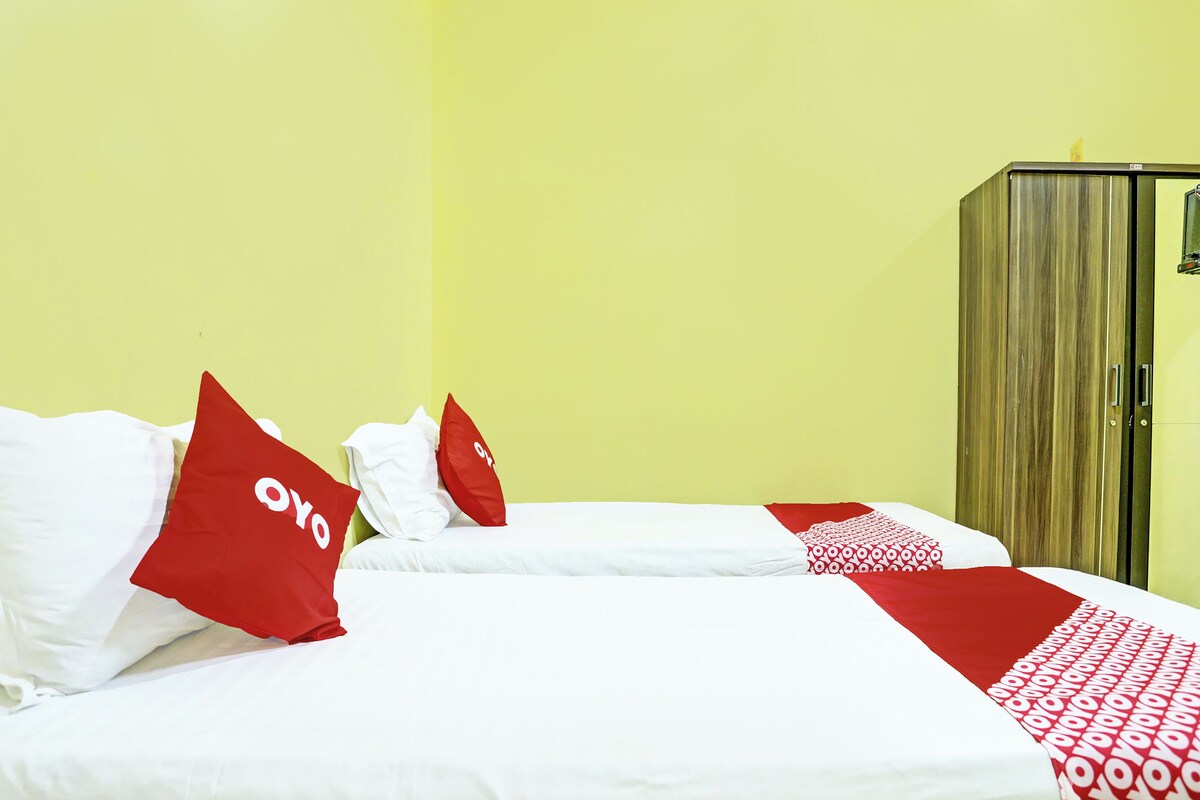 A hotel room with two beds, each with white bedding and red pillows.