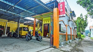 A building with a covered parking area, a signboard, and a yellow vehicle. - OYO 3214 Puri Amalia (Banyuwangi)