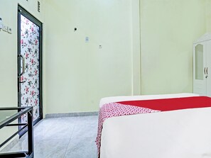 A hotel room with a bed, a wardrobe, a door with a floral pattern, and a tiled floor.