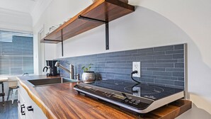 A kitchen with a modern induction cooktop, a built-in oven, and a backsplash of dark tiles. - Newly Renovated Modern Cottage: Walk into Historic Wailuku Town! (Wailuku)