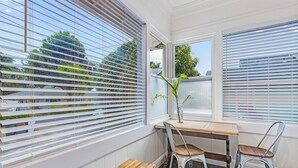 A corner room with a wooden table, two chairs, a bench, and large windows with blinds. - Newly Renovated Modern Cottage: Walk into Historic Wailuku Town! (Wailuku)
