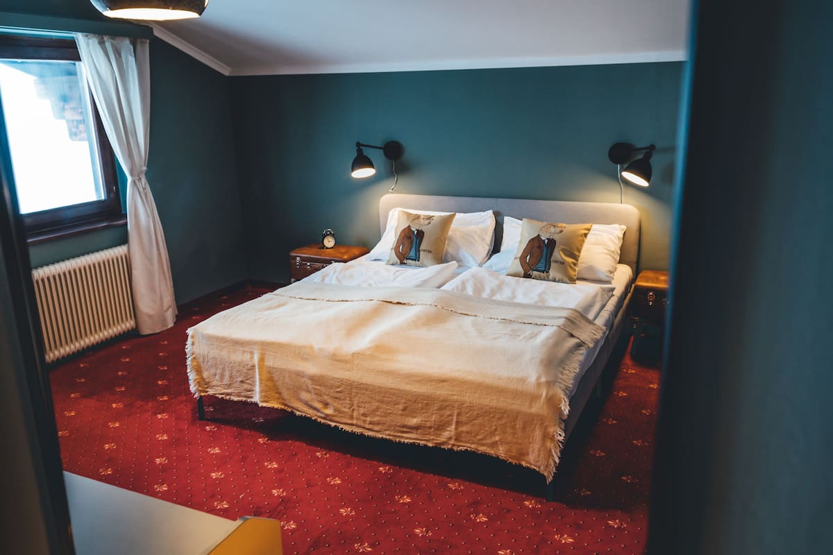 Ein Schlafzimmer mit einem Bett, zwei Nachttischlampen, einem Fenster mit Vorhängen und einer Heizung.