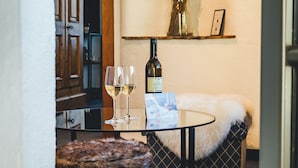 Una habitación pequeña y acogedora con una mesa redonda, un taburete de madera, una botella de vino y un jarrón con plantas secas.