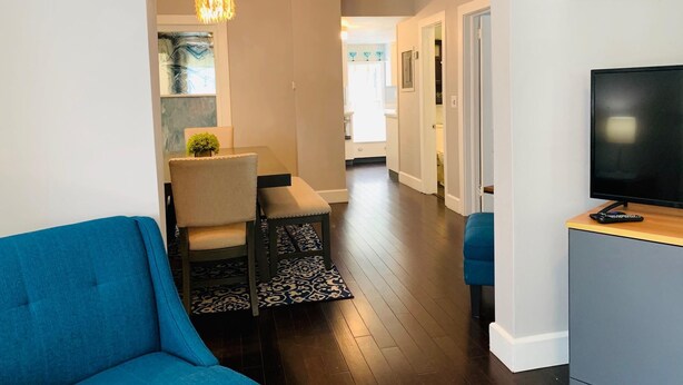 Een moderne woonkamer met een blauwe bank, een eethoek met een tafel en stoelen, en een televisie op een houten kast.